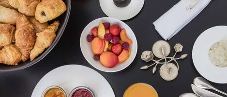 A breakfast spread with croissants, fruit, eggs, and coffee on a table.