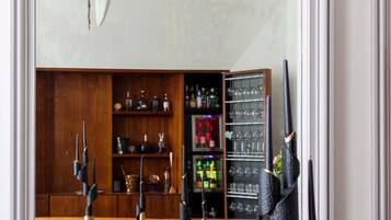 Un comedor con un espejo grande que refleja una araña, muebles de madera y una zona de bar con estantes llenos de botellas y vasos.