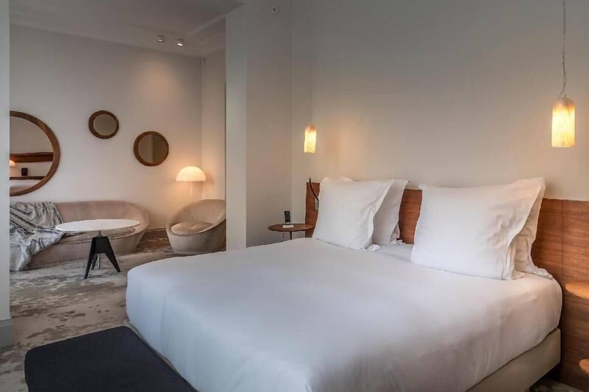 Una habitación de hotel con una cama grande, un espejo redondo, una pequeña mesa redonda y una silla.