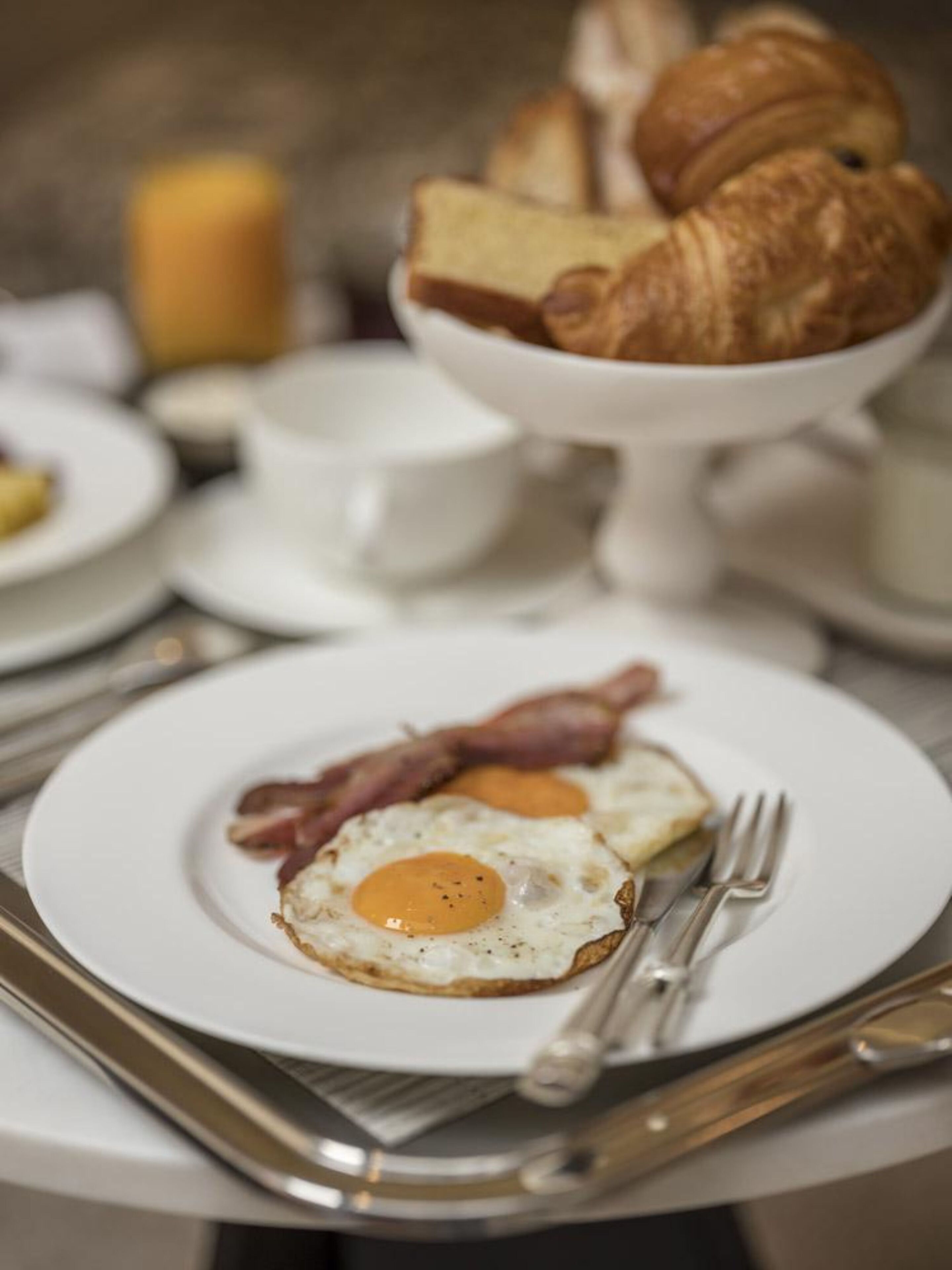 A breakfast setting with a plate of fried eggs, bacon, and croissants.