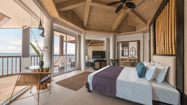 Une chambre spacieuse avec un grand lit, un ventilateur de plafond et une vue sur la mer.