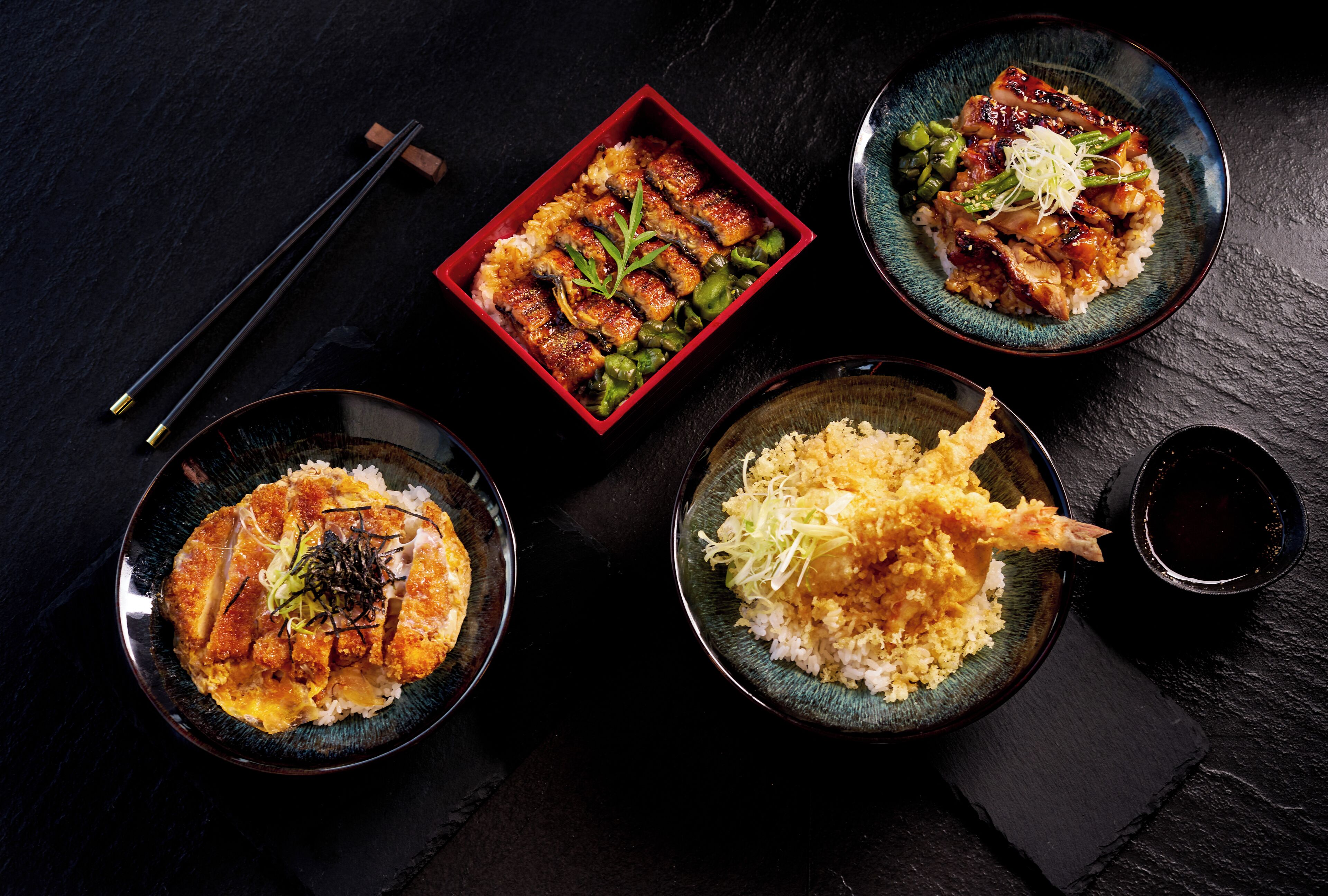 A table with four dishes, chopsticks, and a small bowl of soy sauce.