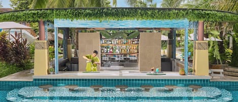 A poolside bar with a tropical setting, including a pool with a mosaic tile design and a covered seating area with greenery overhead.