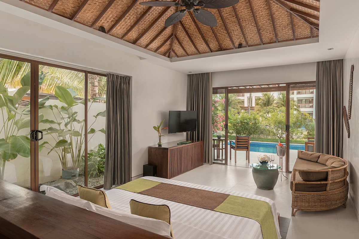 Een moderne hotelkamer met een groot bed, een televisie, een balkon met uitzicht op het zwembad en een plafondventilator.