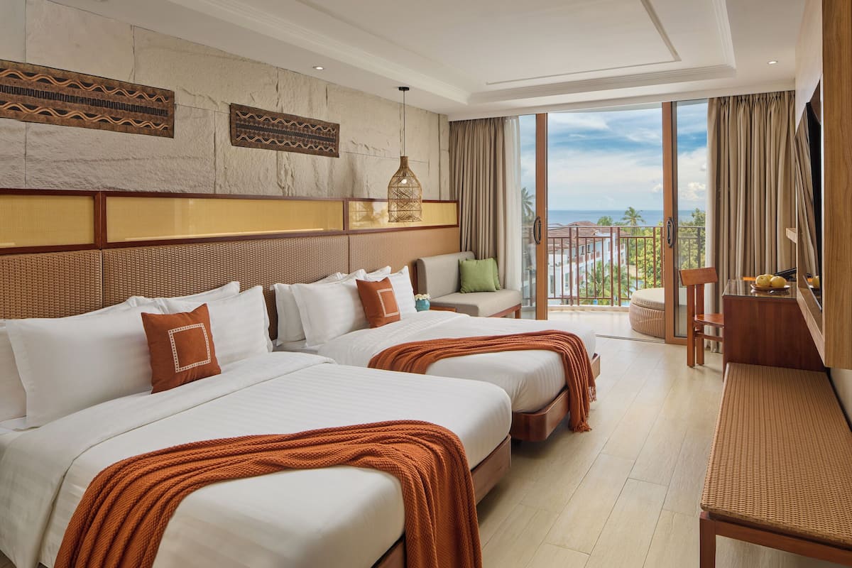 Een hotelkamer met twee bedden, een bank, een bureau en een balkon met uitzicht op de oceaan.