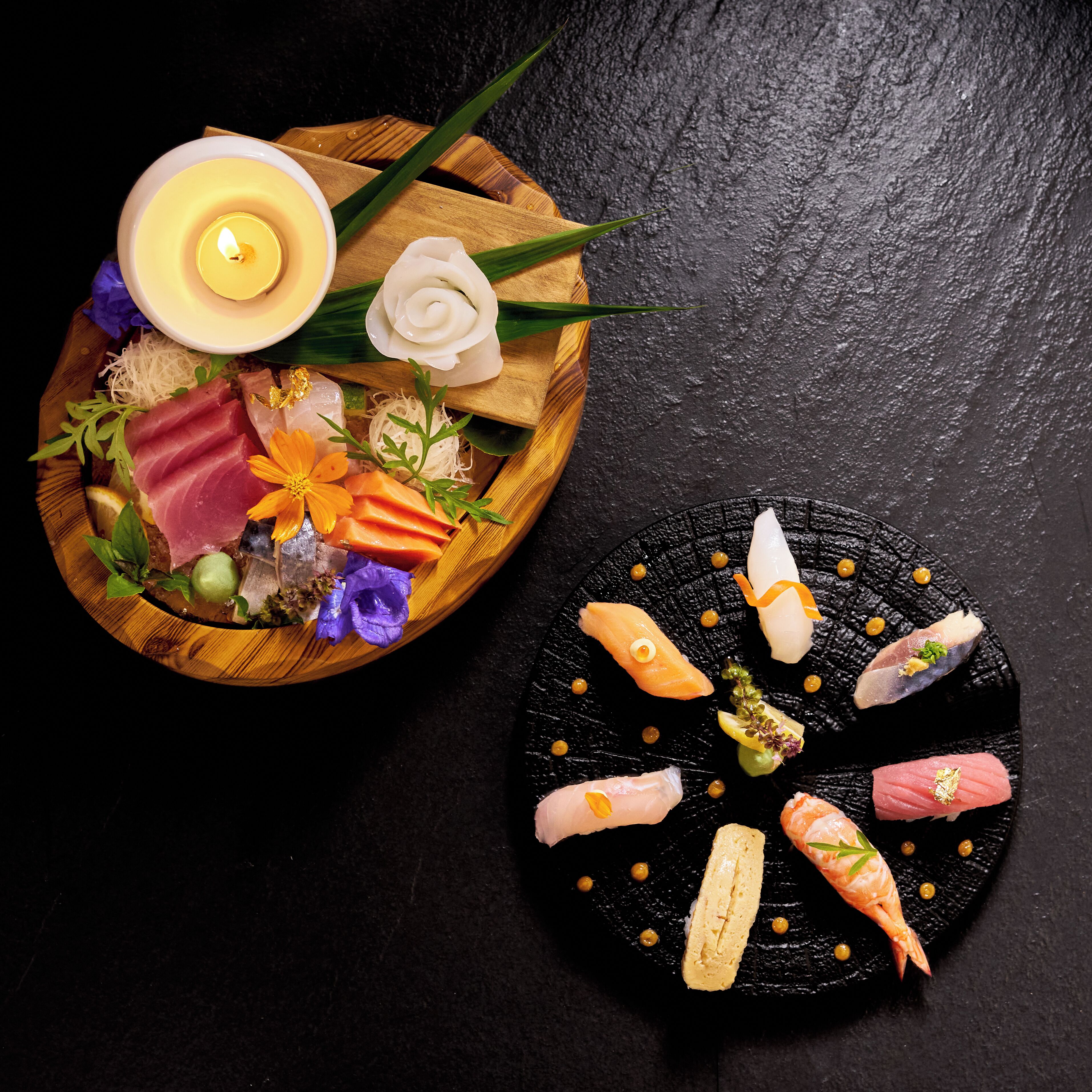Un plateau en bois contenant différentes sortes de sushis et une bougie, posé sur une surface sombre.