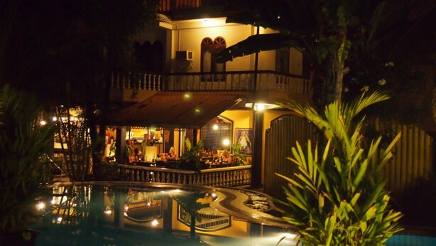 A two-story building with a bar area on the ground floor, a pool, and a covered seating area with plants. - Hotel Flower Garden (Unawatuna)