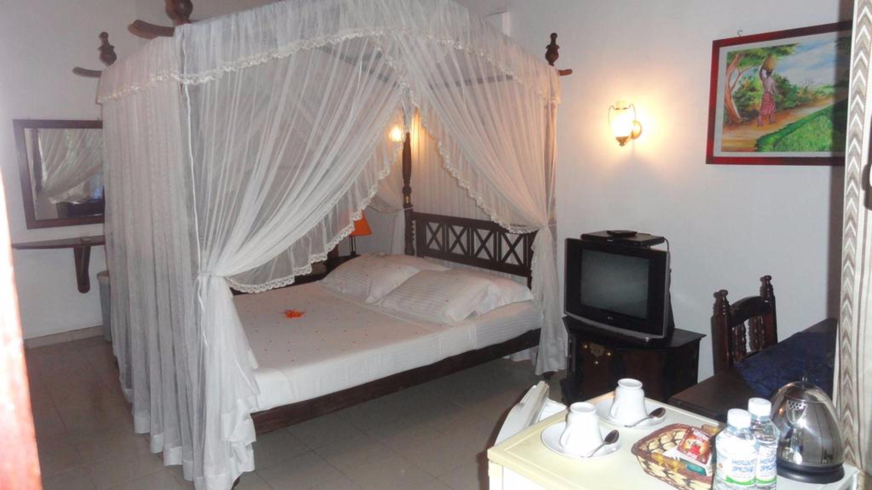 A room with a four-poster bed, a television, and a dining table with cups and bottles.