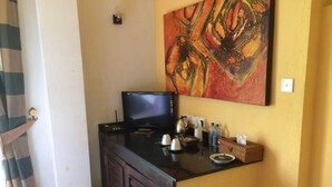 A hotel room with a flat-screen TV on a black cabinet, a painting on the wall, and a small table with toiletries. - Hotel Flower Garden (Unawatuna)