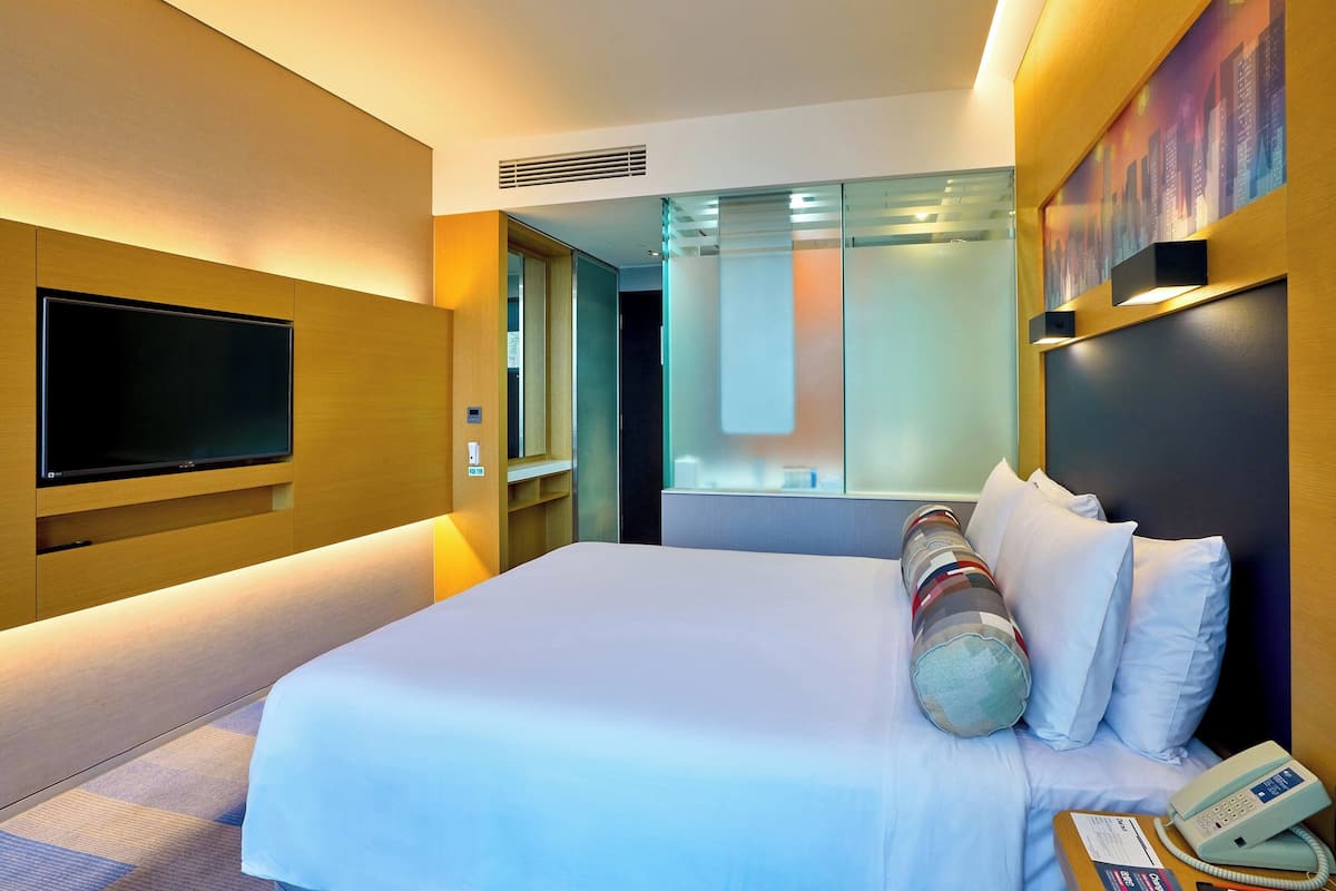 Ein Hotelzimmer mit einem großen Bett, einem flachbildfernseher an der Wand, einem Nachttischtelefon und einem Stadtbild.