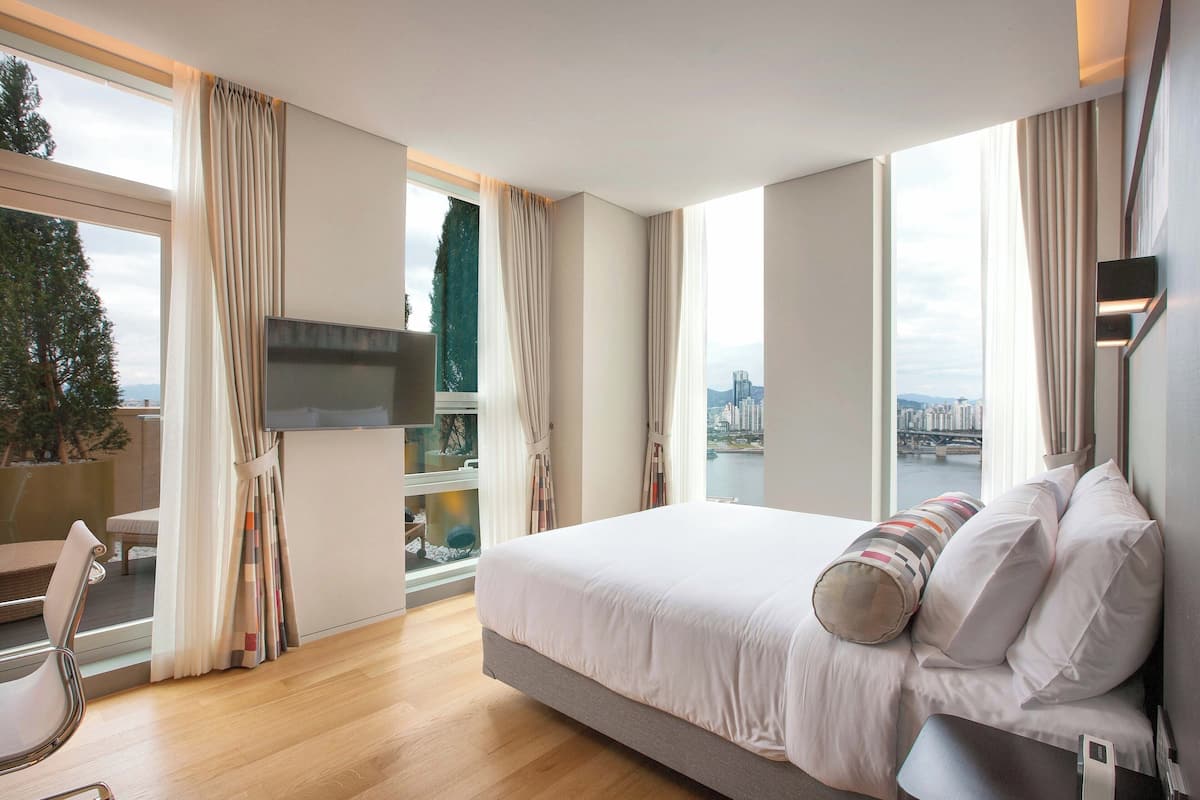 Ein modernes Hotelzimmer mit einem großen Bett, einem Flachbildfernseher, Blick auf die Stadt und einem Balkon mit einem Stuhl.
