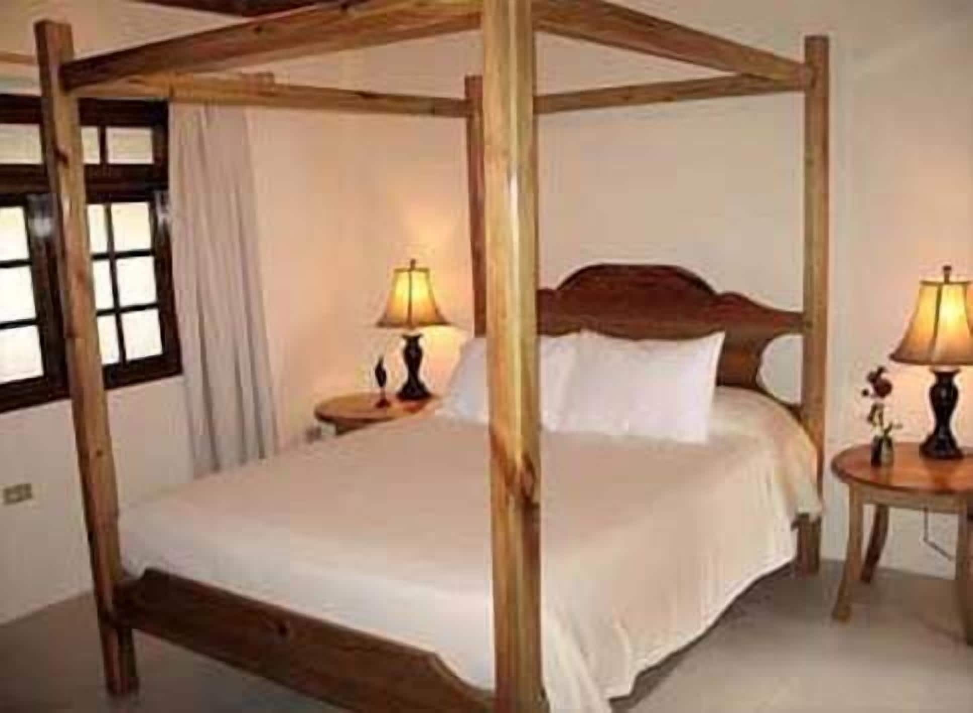 A four-poster bed with a wooden frame and white bedding. There are two bedside tables with lamps on either side of the bed.