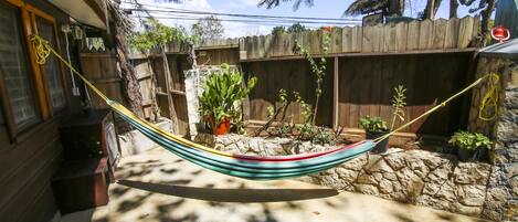 A hammock tied between two wooden posts in a backyard with a stone wall, potted plants, and a wooden fence.