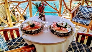 Una mesa dispuesta con dos pasteles decorados, un florero con flores y vista al océano.