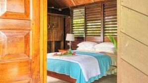 Una habitación de madera con una cama, una mesita de noche y una ventana con persianas.