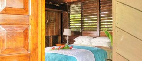 A wooden room with a bed, a nightstand, and a window with blinds.