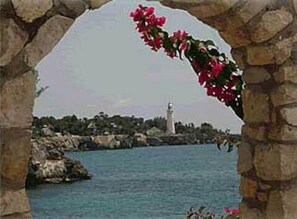 A stone archway framing a coastal view with a lighthouse in the distance.