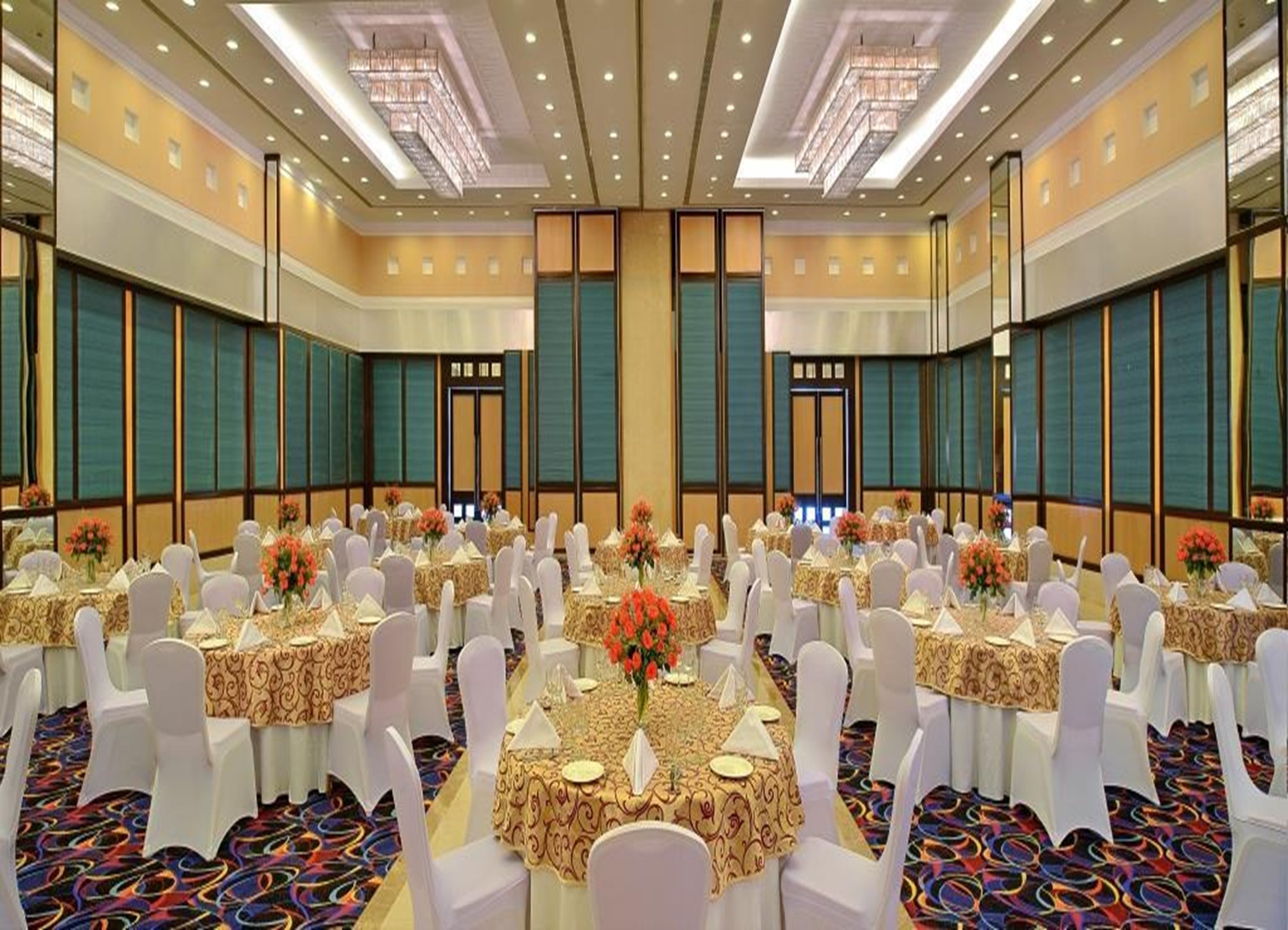 Un amplio salón de conferencias con mesas redondas, sillas blancas y centros de mesa florales.