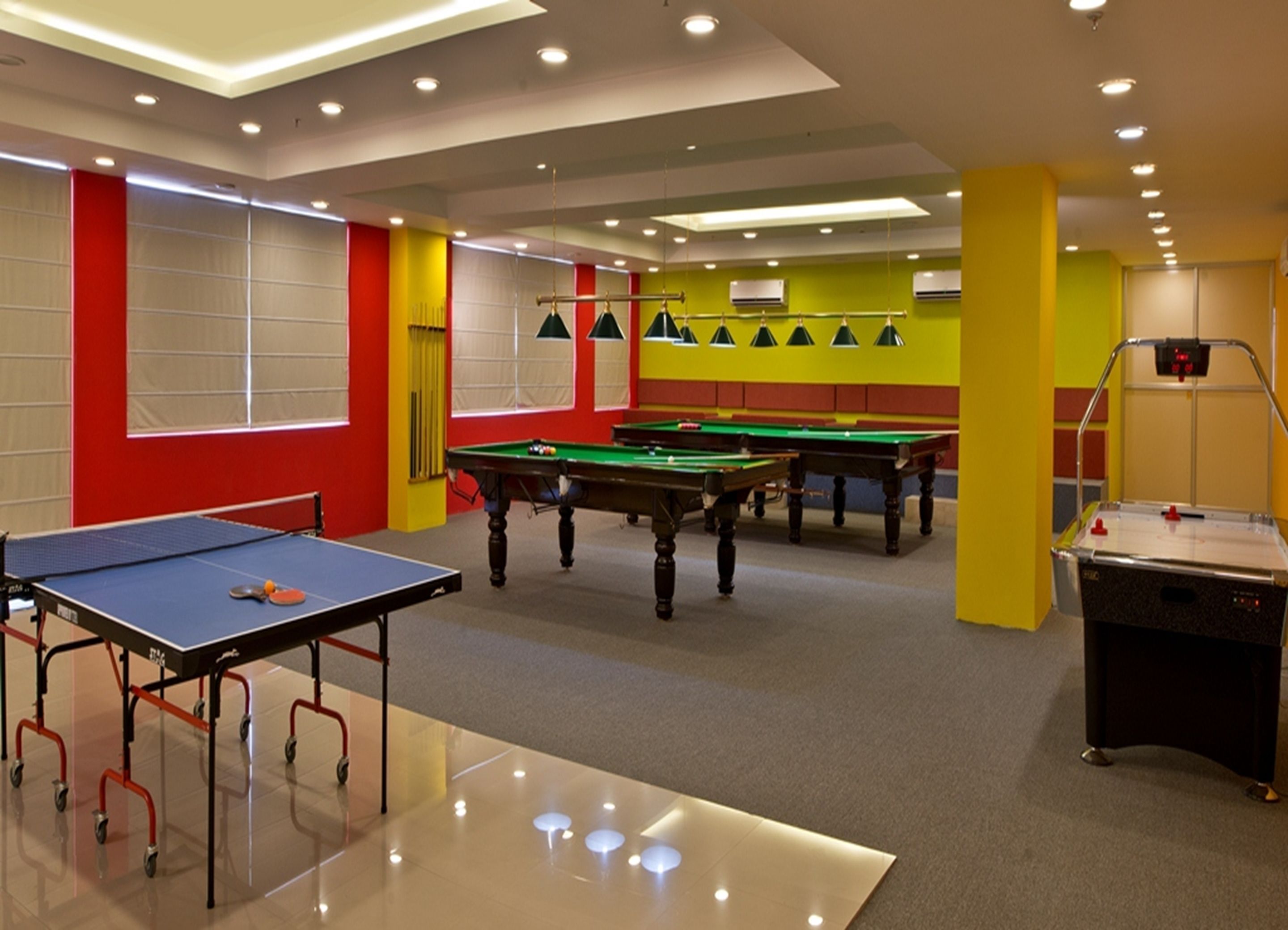A room with a ping pong table, pool tables, and a foosball table.