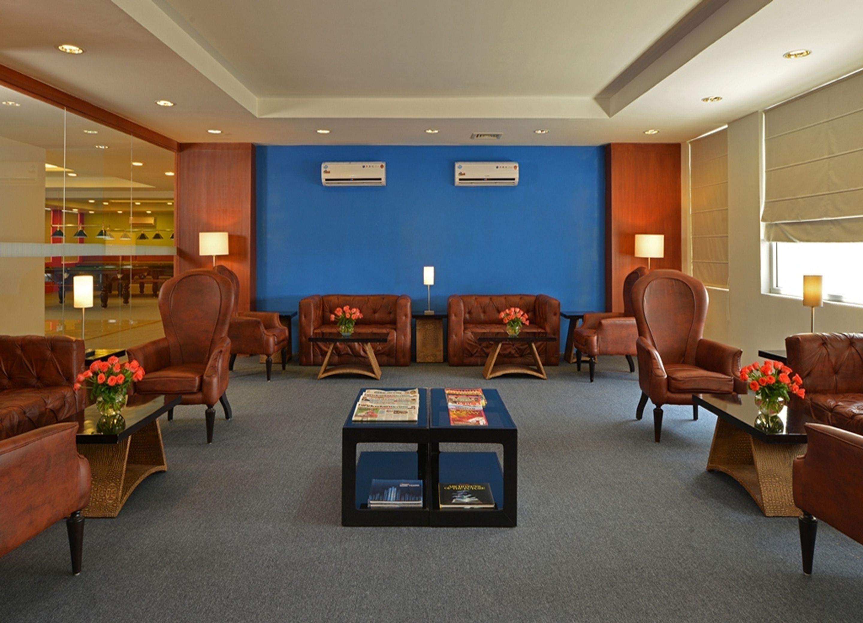 A lobby with leather sofas, a coffee table with magazines, and two air conditioning units on the wall.