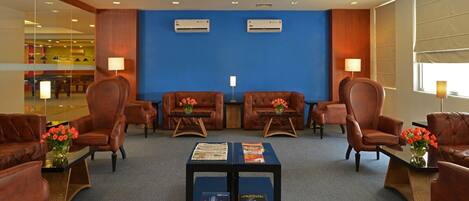 A lobby with leather sofas, a coffee table with magazines, and two air conditioning units on the wall.