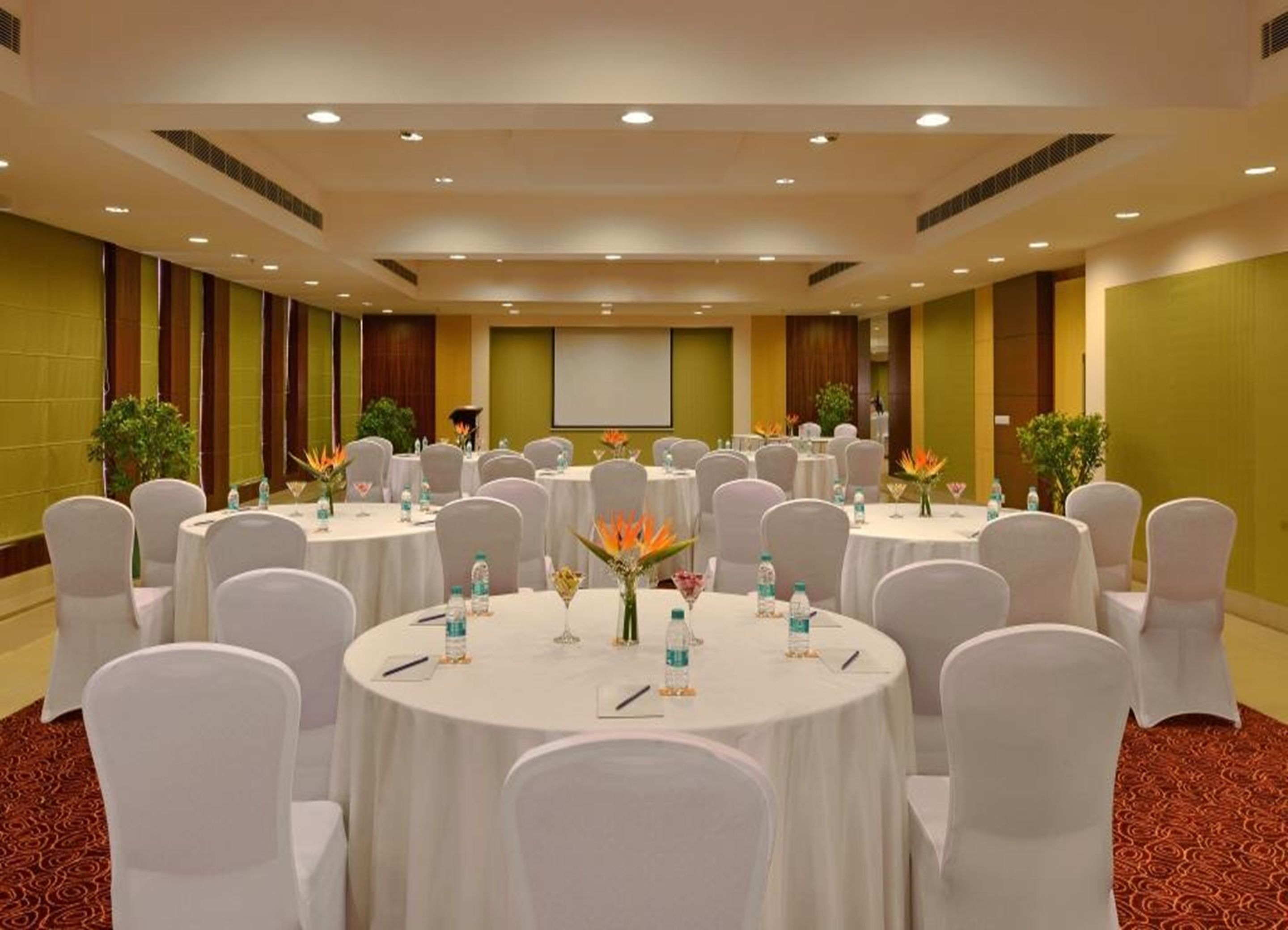 A conference room with multiple round tables, white chairs, and floral centerpieces.