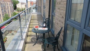A balcony with a table and chairs, a bottle of wine, and a bowl of fruit.