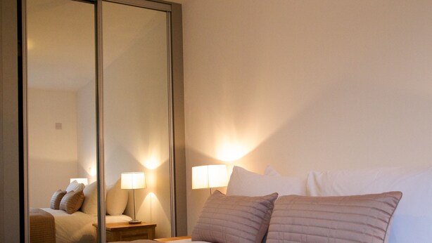 A hotel room with a large bed, bedside lamps, and a mirror reflecting the room.