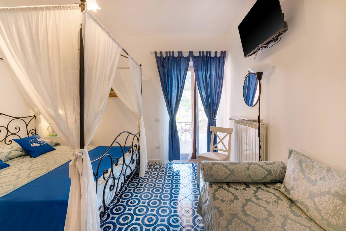 Un dormitorio con cama, sofá, televisor montado en la pared y ventana con cortinas.