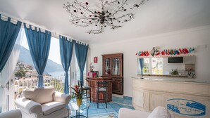 A living room with a view of the sea, a wooden cabinet, and a bar area with flags.