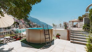 A pool area with a ladder, outdoor furniture, and a view of a hillside town.