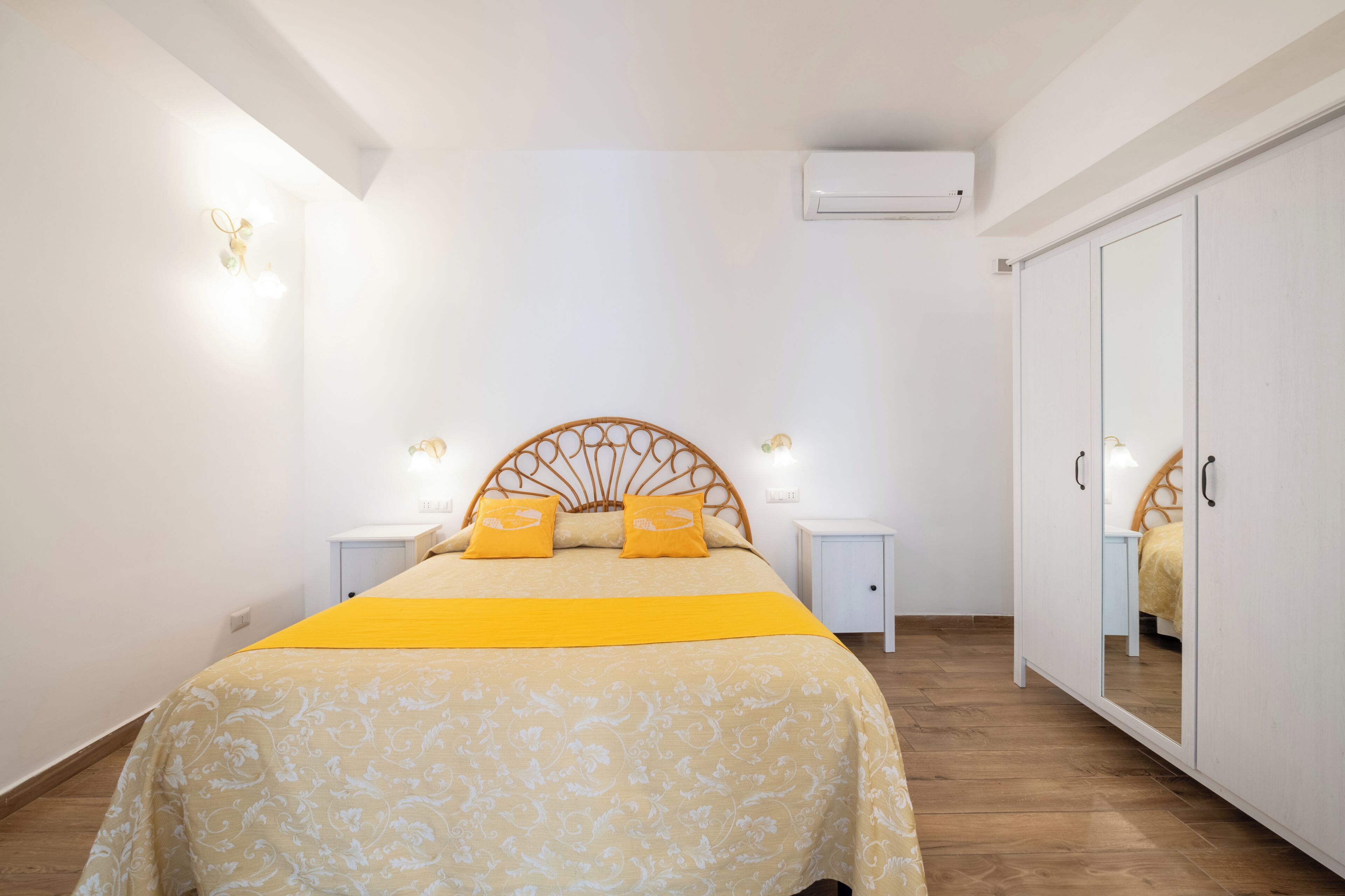 A bedroom with a bed, bedside tables, a wardrobe, and an air conditioning unit.