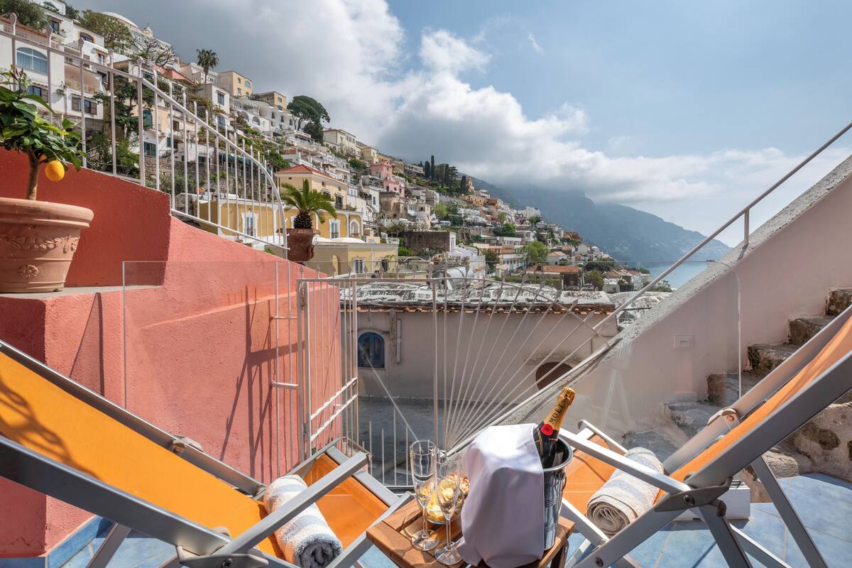 Una terraza con vistas a un pueblo en la ladera, una botella de champán y una copa de vino.