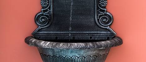 A wall-mounted, ornate black metal water spigot with a decorative top and a textured base.