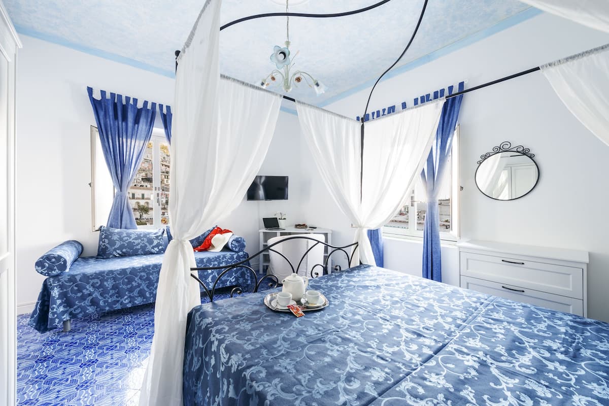Un dormitorio con cama, mesita de noche, televisor y ventana con cortinas.