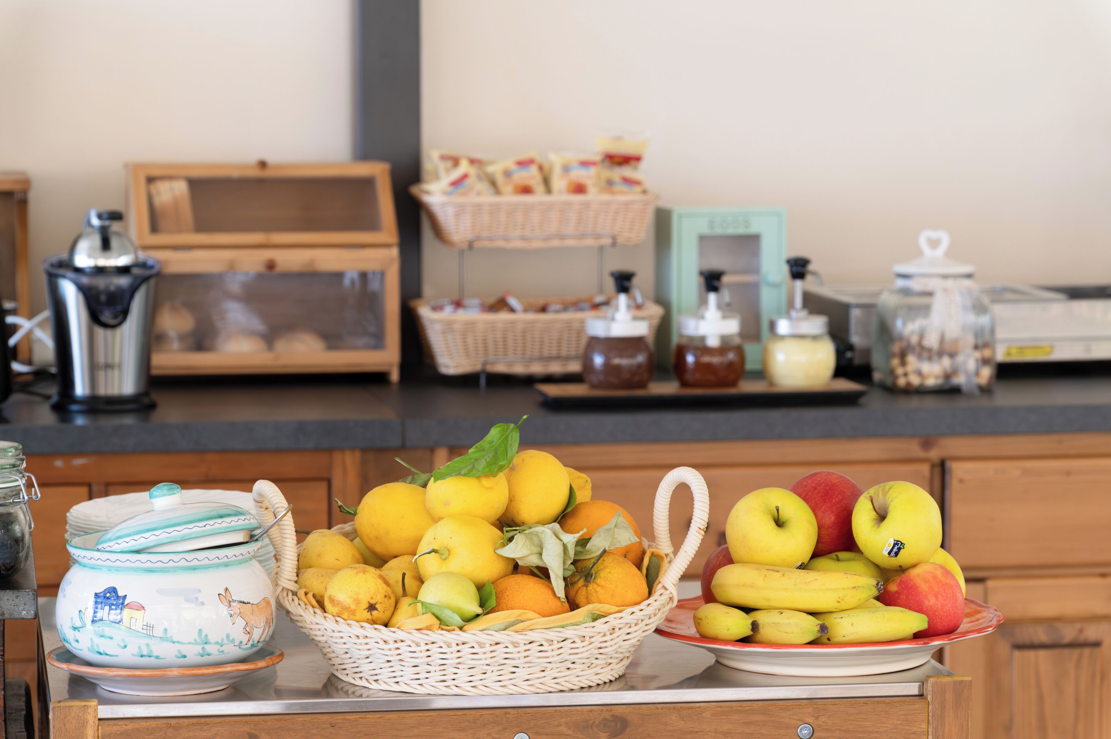 A kitchen counter with a basket of fruits, a ceramic pot, and various kitchen items.