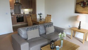 A living room with a grey sofa, a wooden coffee table, and a small table with a lamp. - Citystay Living - Warren Close (Cambridge)