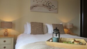 A hotel room with a bed, two bedside tables, a nightstand, a lamp, a tray with food, and a painting on the wall. - Citystay Living - Warren Close (Cambridge)