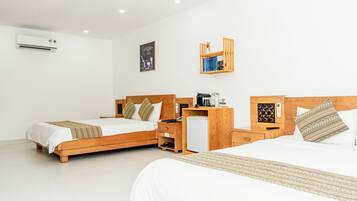 A hotel room with two wooden beds, a small desk with a coffee maker, a refrigerator, and a shelf with books and a decorative item.