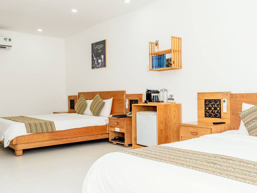 Una habitación de hotel con dos camas de madera, un escritorio pequeño con una cafetera, un refrigerador y un estante con libros y un objeto decorativo.