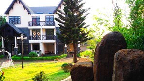 Un edificio de dos pisos con un balcón, un jardín con un estanque y un columpio.