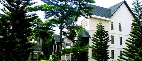 A building with a white facade and dark roof, surrounded by well-maintained greenery and a clear sky.