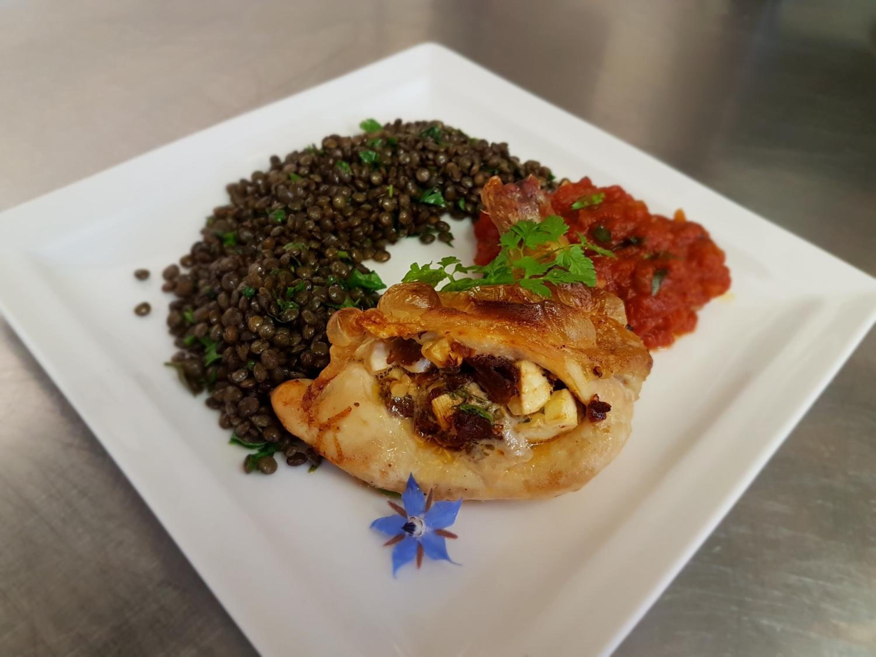 A plate with a stuffed chicken breast, lentils, and a tomato-based sauce.