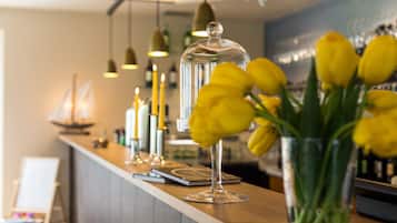 Zona de bar con una vitrina de cristal, un florero con flores amarillas y lámparas colgantes.