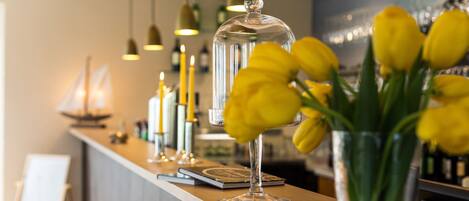 A bar area with a clear glass display case, a vase with yellow flowers, and hanging pendant lights.