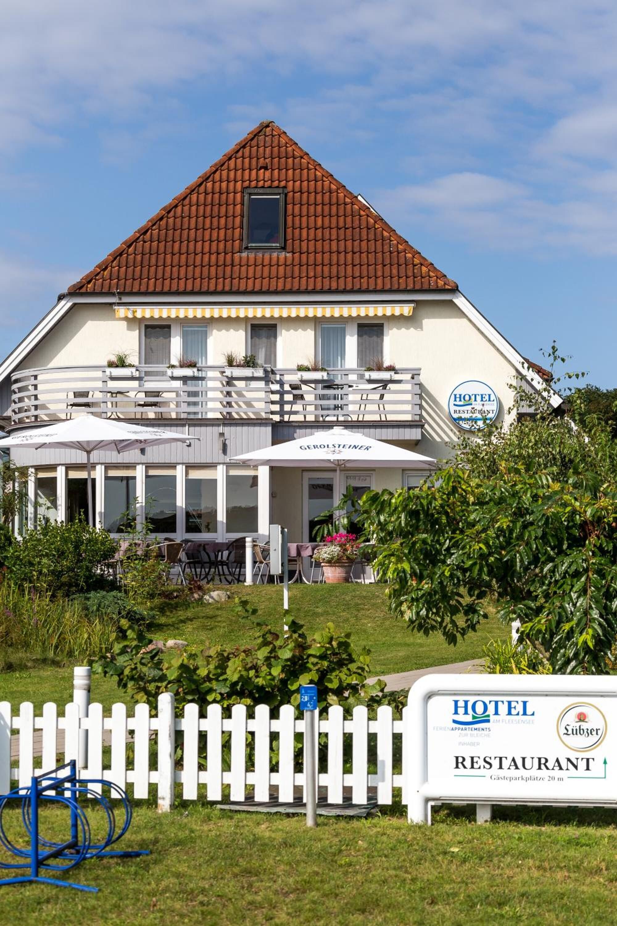 Ein Hotel mit rotem Ziegeldach, einem Balkon mit Sitzgelegenheiten und einem Schild, das es als Hotel und Restaurant kennzeichnet.