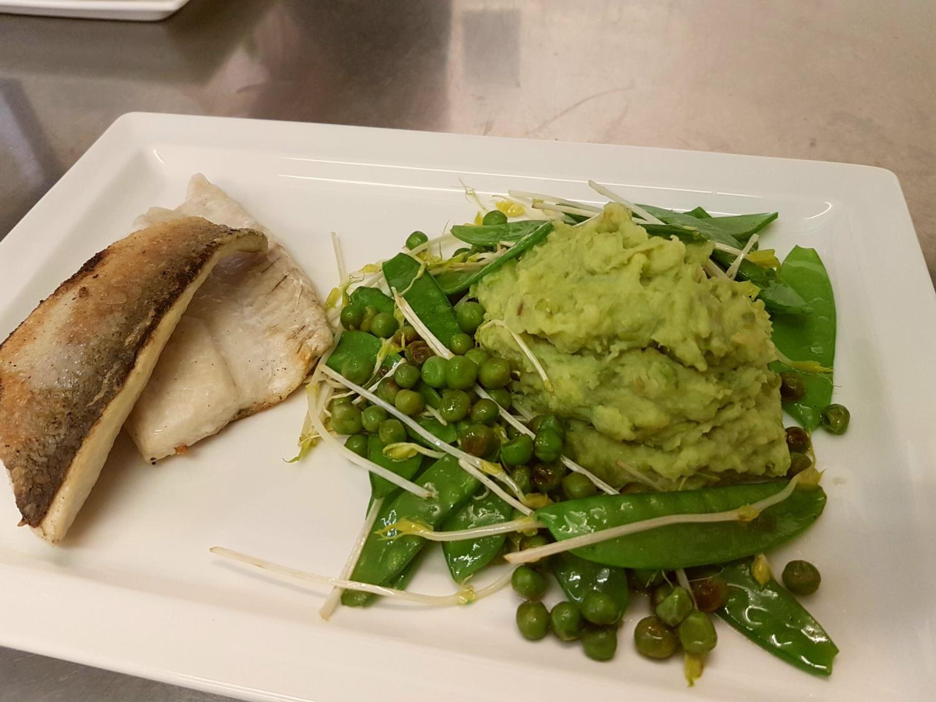 Ein Teller mit gegrilltem Fisch, grünen Erbsen und Kartoffelpüree.