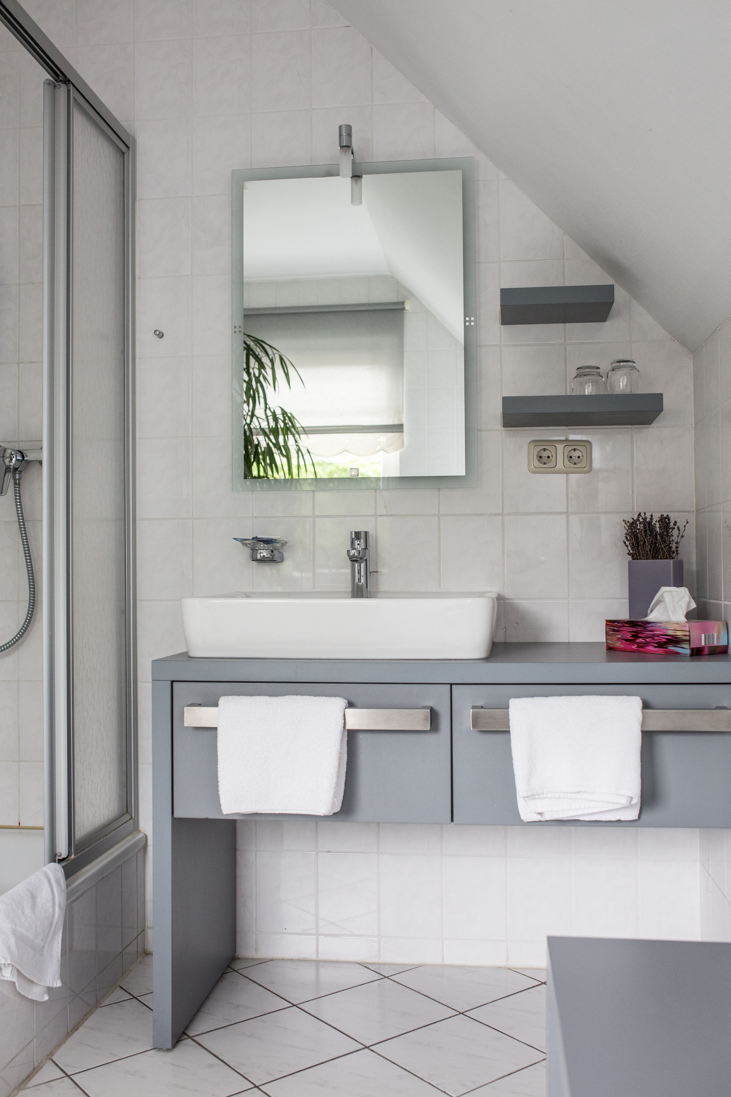 Une salle de bain moderne avec une douche à parois de verre, un lavabo blanc et un meuble-lavabo gris.