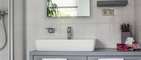 A modern bathroom with a glass shower enclosure, a white sink, and a grey vanity.