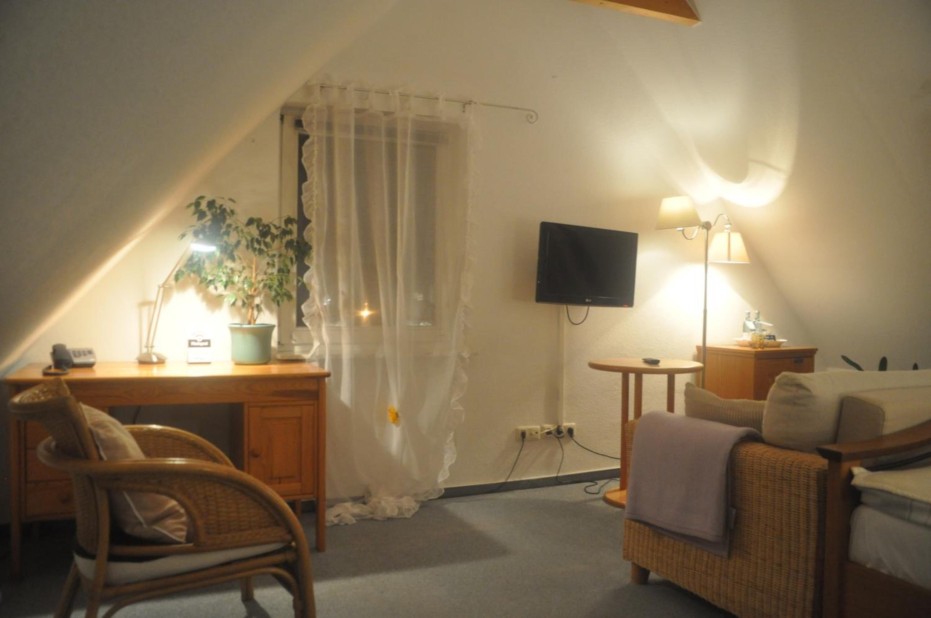 A cozy room with a wooden desk, a chair, a bed, a TV, and a lamp.